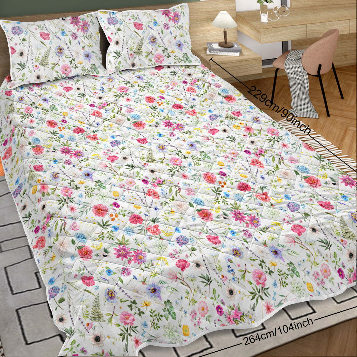 Floral patterned bedspread on a bed with pillows and a desk in the background.