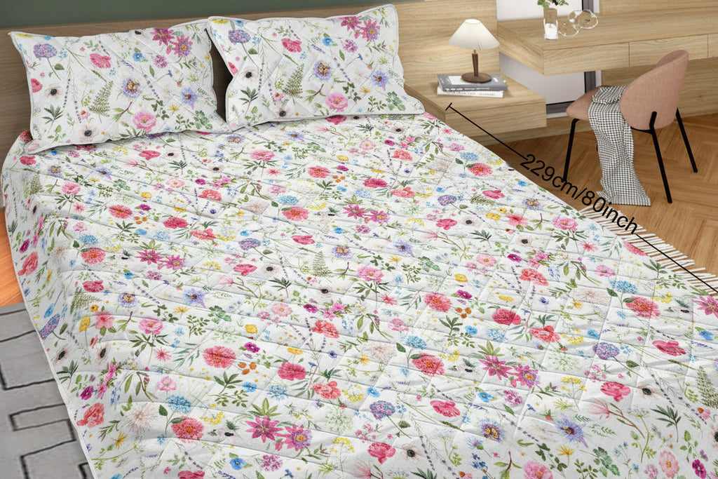 Floral patterned bedspread on a bed with pillows and a desk in the background.