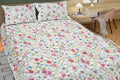 Floral patterned bedspread on a bed with pillows and a desk in the background.